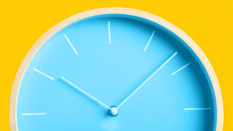 A blue analog clock against a yellow background. The time is 10:08.