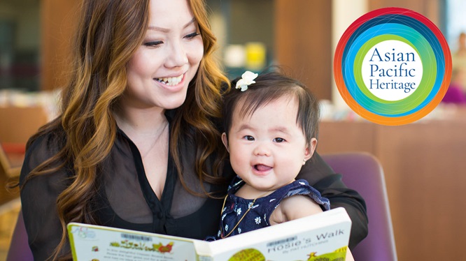 A mother has a baby in her lap. She is reading to the baby from a board book.
