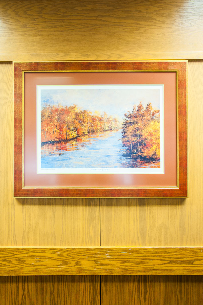 Framed print of a river with trees on both banks shown hanging on a wall